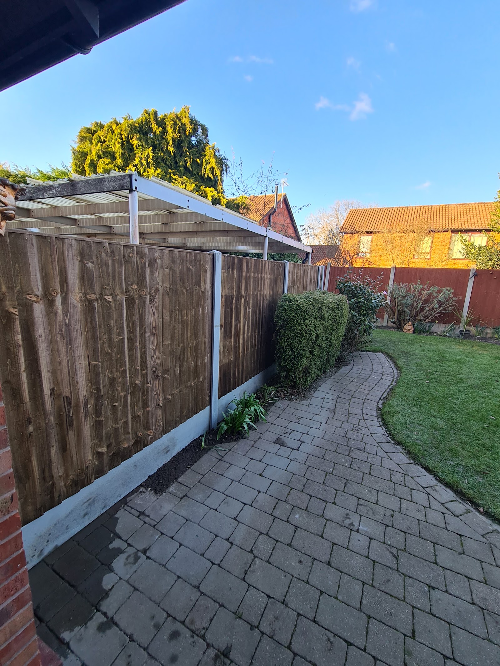 A run of newly installed feather edge fence panels with framed edges beside a block-paved garden path