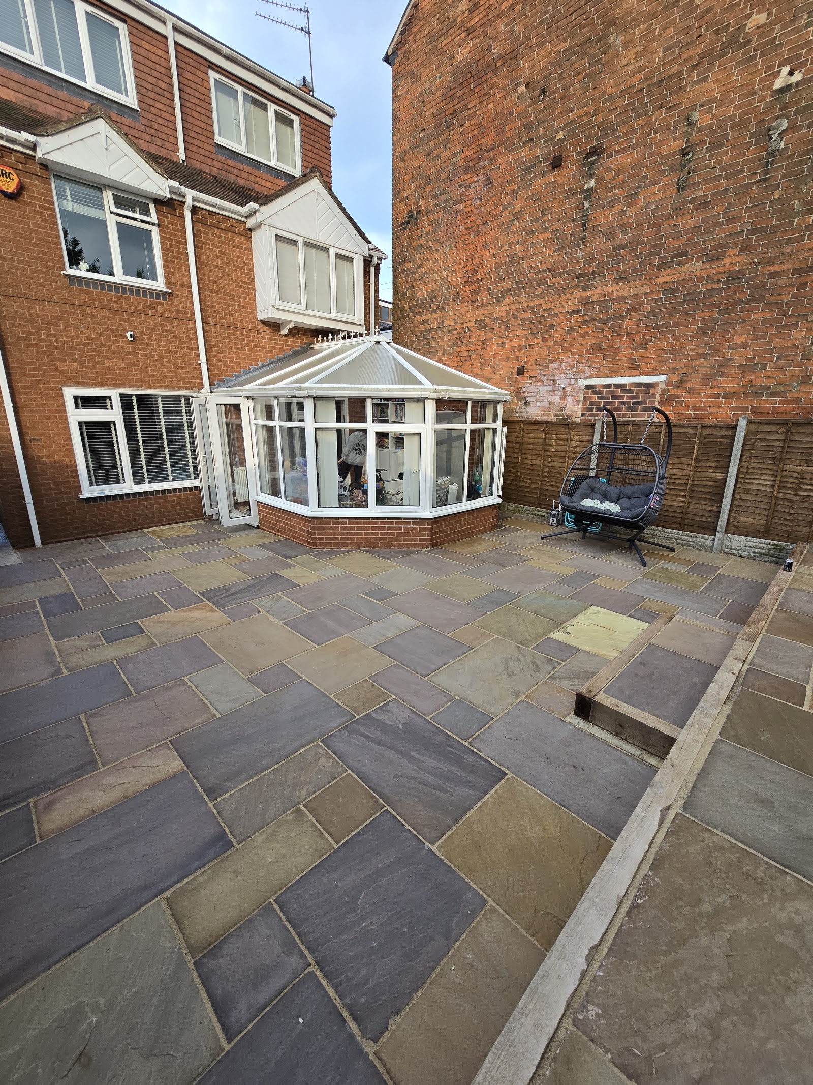 A large Indian sandstone patio in mixed grey tones laid behind a house with a conservatory in Solihull